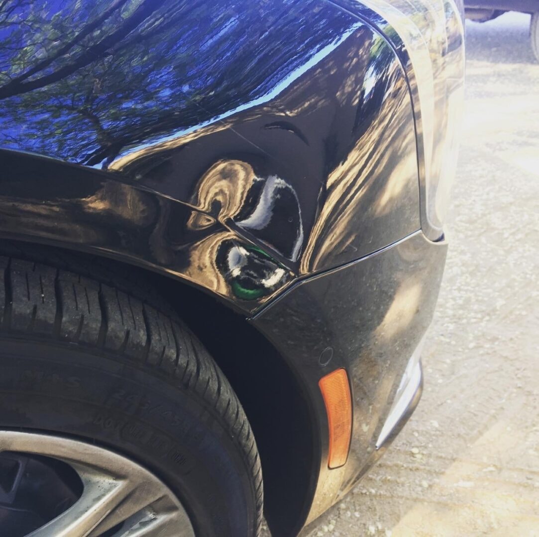 Black car fender with large crease dent before paintless dent repair