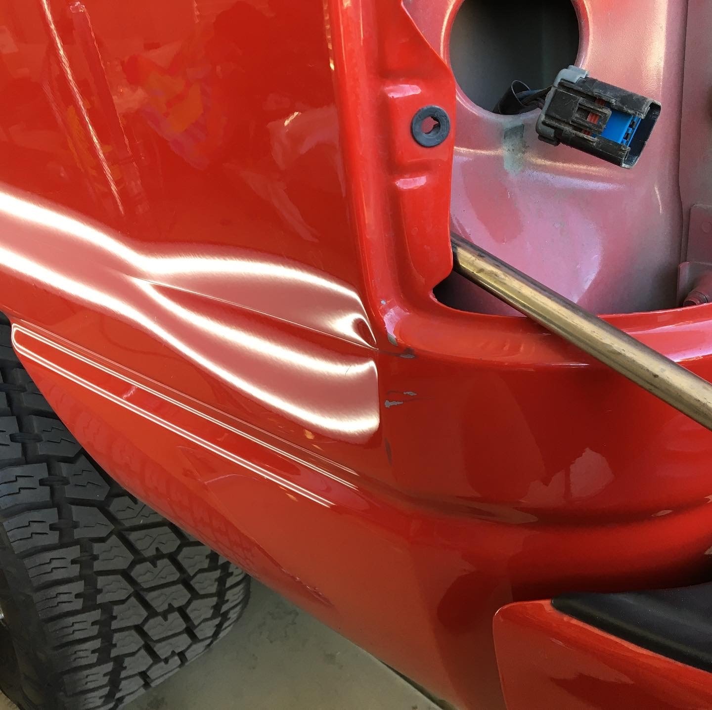 Red truck door panel with crease dent before paintless dent repair