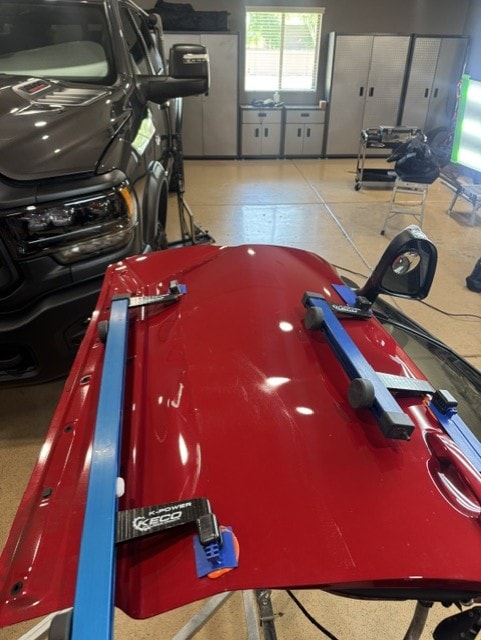 Red car door panel on workbench with PDR repair bars