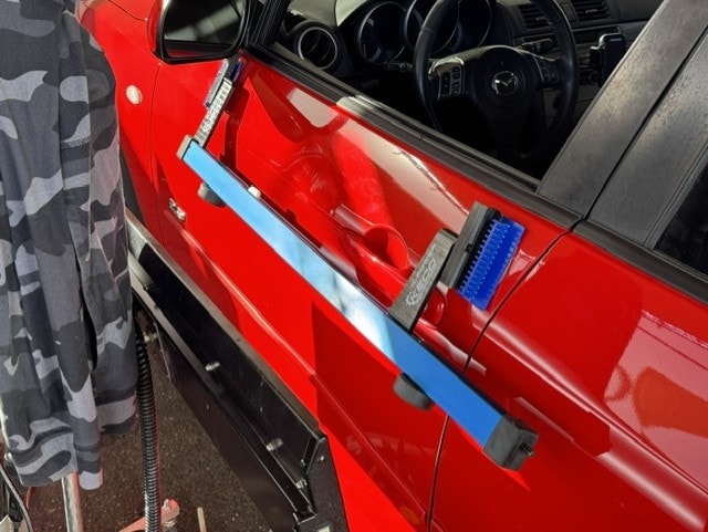 PDR tools attached to red Mazda door panel during repair