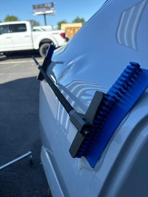 Blue PDR glue pull tabs attached to white car panel outdoors